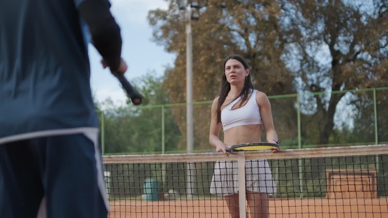 코치와 함께 야외 코트에서 테니스를 연습하는 젊은 여성. 코치는 선수가 그녀의 기술에 대해 일하면서, 운동 훈련 세션에서 그녀의 스트로크를 완성하는 동안 지침을 제공합니다.