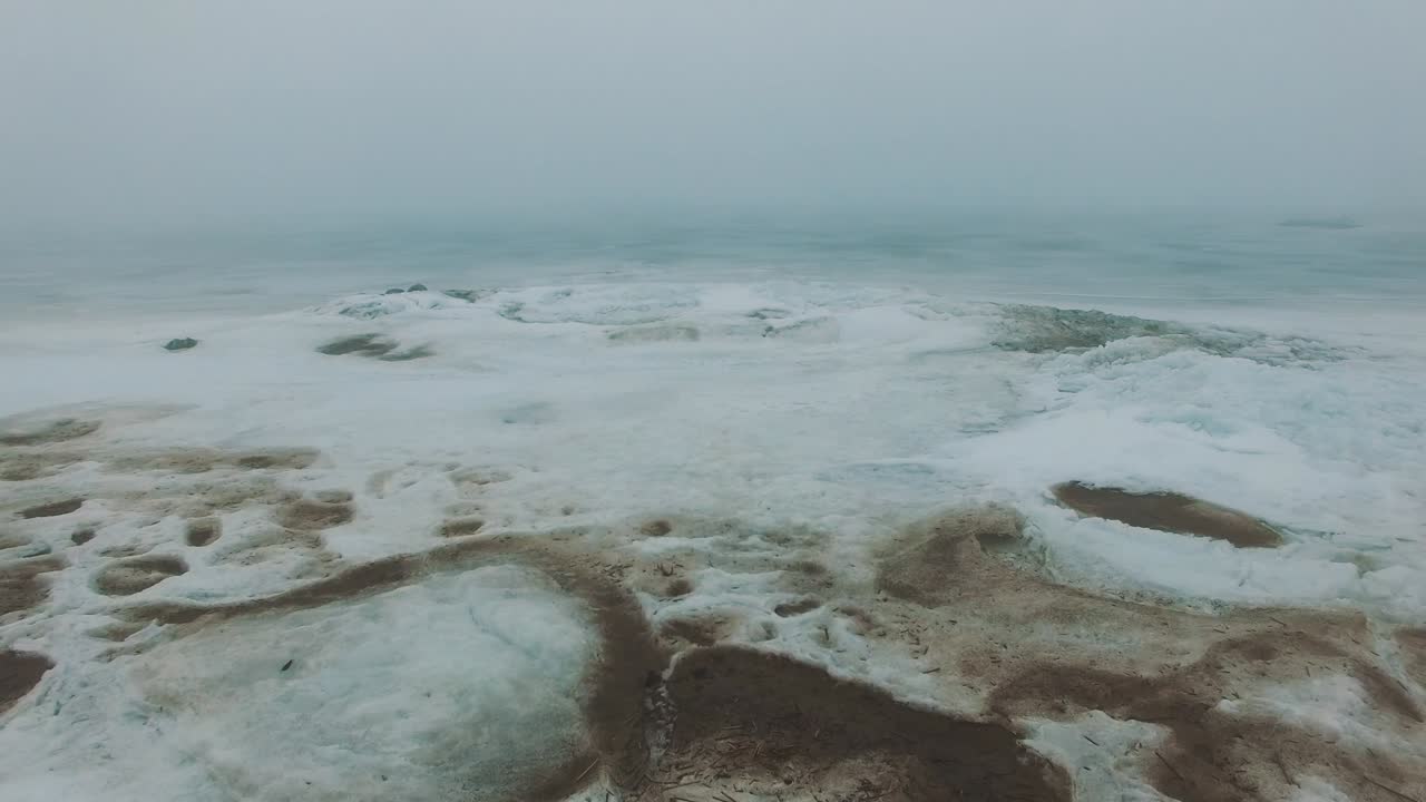 얼어붙은 바다 해안선 위를 날아다니며 안개와 안개가 가득한 추운 겨울 날에 얼음 균열이 있습니다.