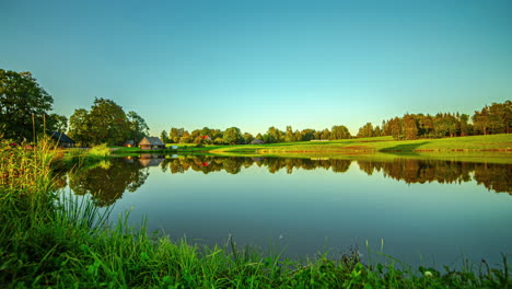 Smooth-timelapse-of-tree-shadows-passing-over-pond-and-grassy-field-as-day-turns-to-blue-hour