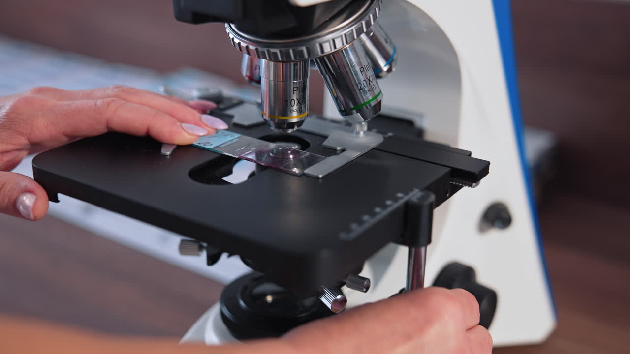 Scientific laboratory microscope examining drop. Close up shot of sample slide and microscope with metal lens at laboratory