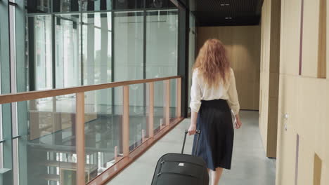 an unrecognizable businesswoman walks backwards with a trolley. she is on his way to an important business trip.