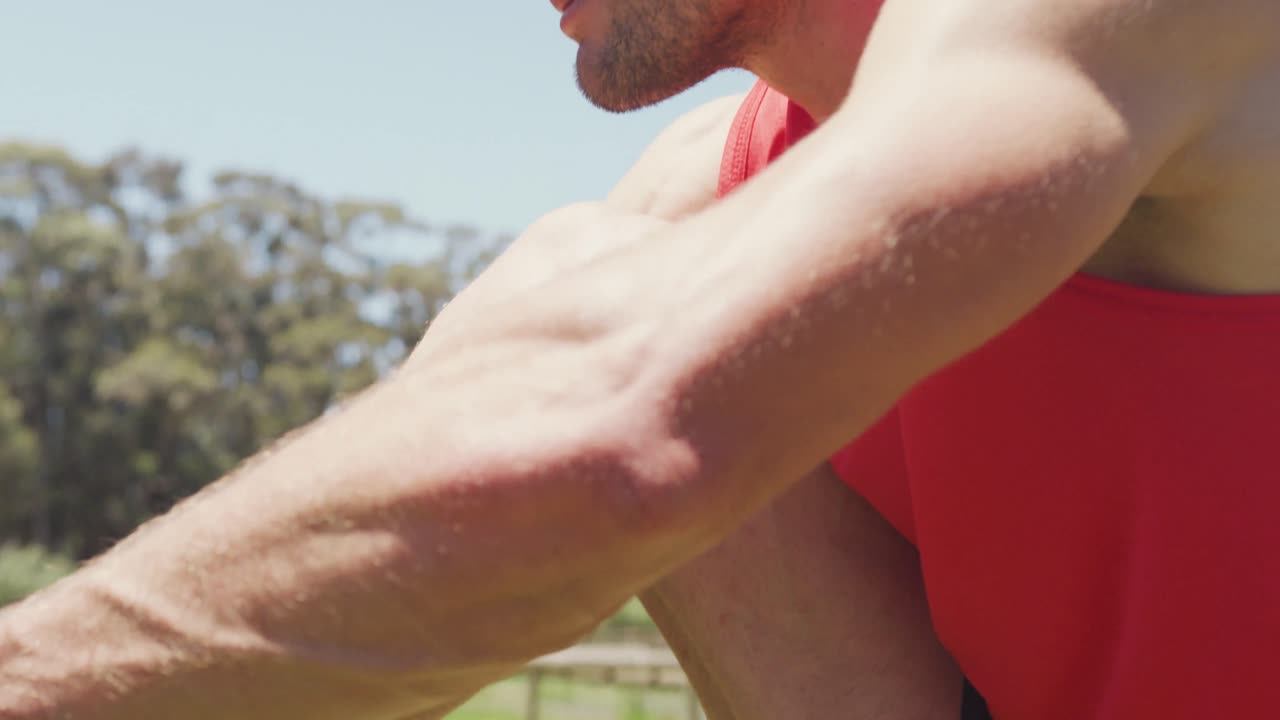 Hombre caucásico en forma, con ropa deportiva, atándose el zapato, sentado al aire libre bajo el sol, preparándose para hacer ejercicio