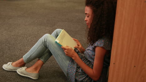 focused student reading a book lying  on the floor