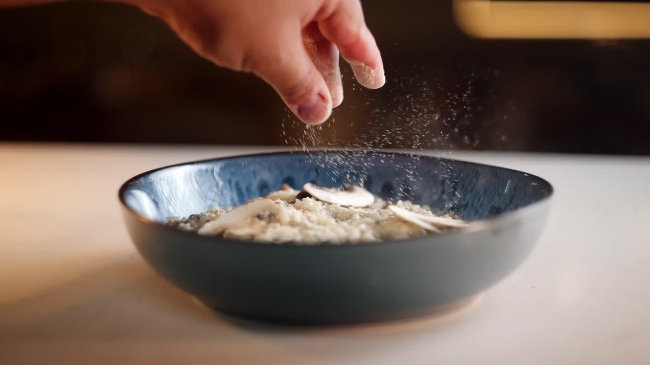 Close up view in slow motion of a Chef spreading grated parmesan cheese over smoky risotto porcini funghi dish under a beautiful and moody atmosphere.