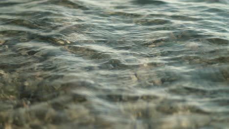 Gentle-wave-ripples-washing-over-beach,-shallow-pebbles