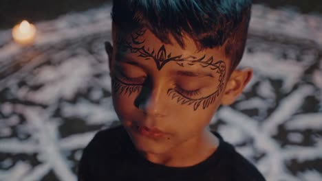 portrait of a concentrating child with closed eyes and face painting during a spiritual ceremony with a candle and white drawings on the ground