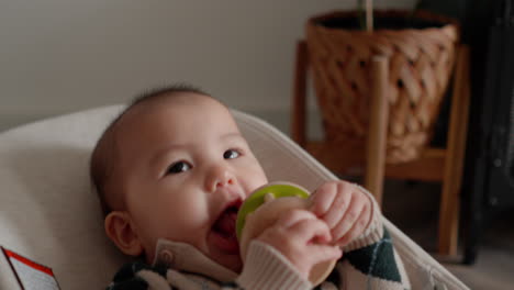 cute asian baby in baby bouncer chewing teething toy, smiling and being happy