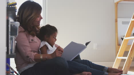 abuela y nieta hispanas sentadas en el suelo del dormitorio de los niños leyendo un libro juntas