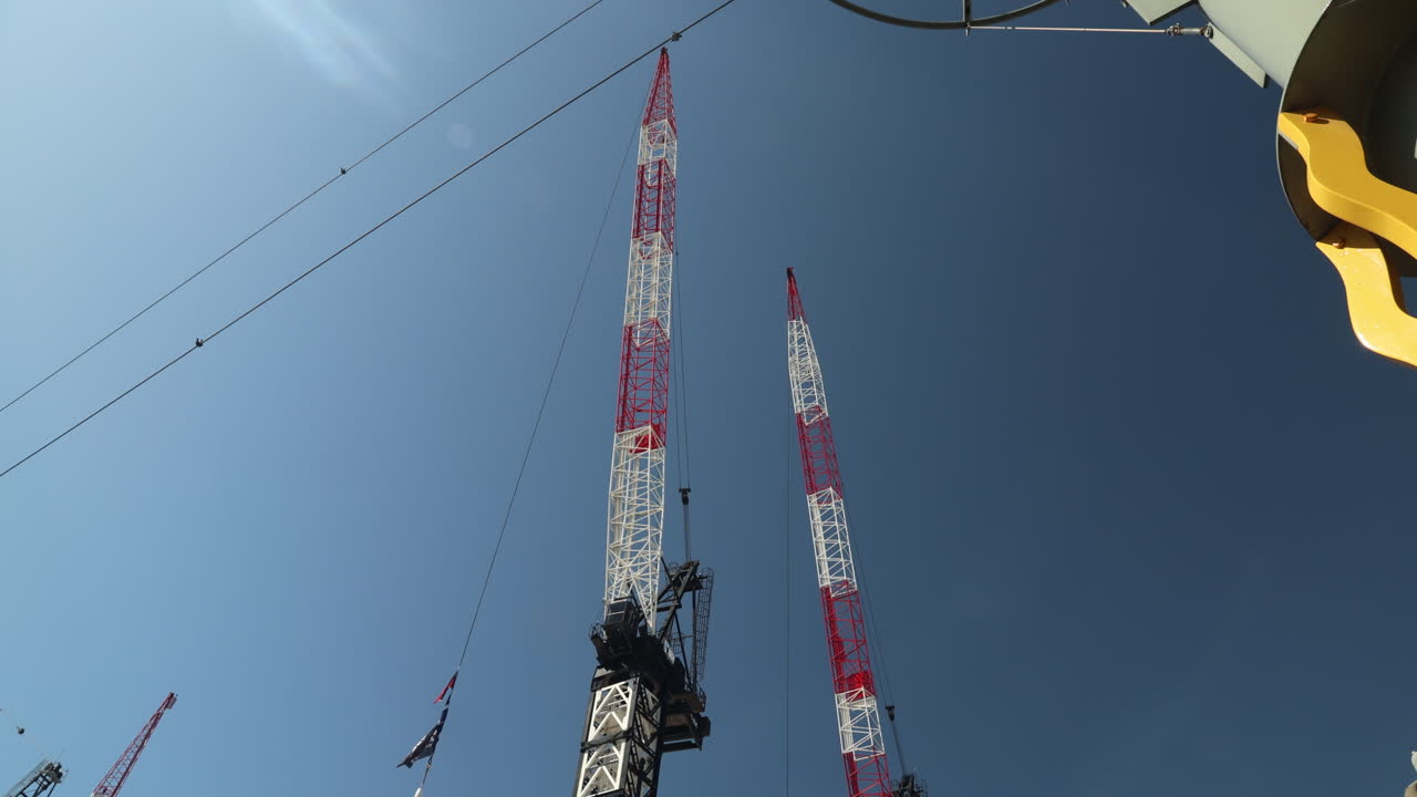 A tilt-up shot of two construction cranes against a bright blue sky. Perfect for projects involving building, development, architecture, engineering, and urban growth.