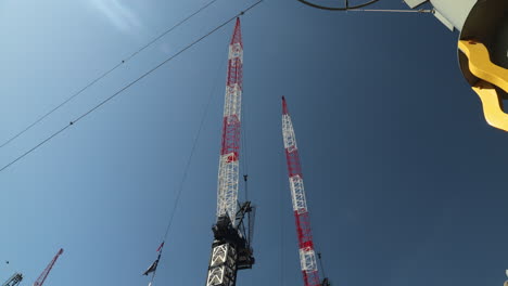 a tilt-up shot of two construction cranes against a bright blue sky. perfect for projects involving building, development, architecture, engineering, and urban growth.