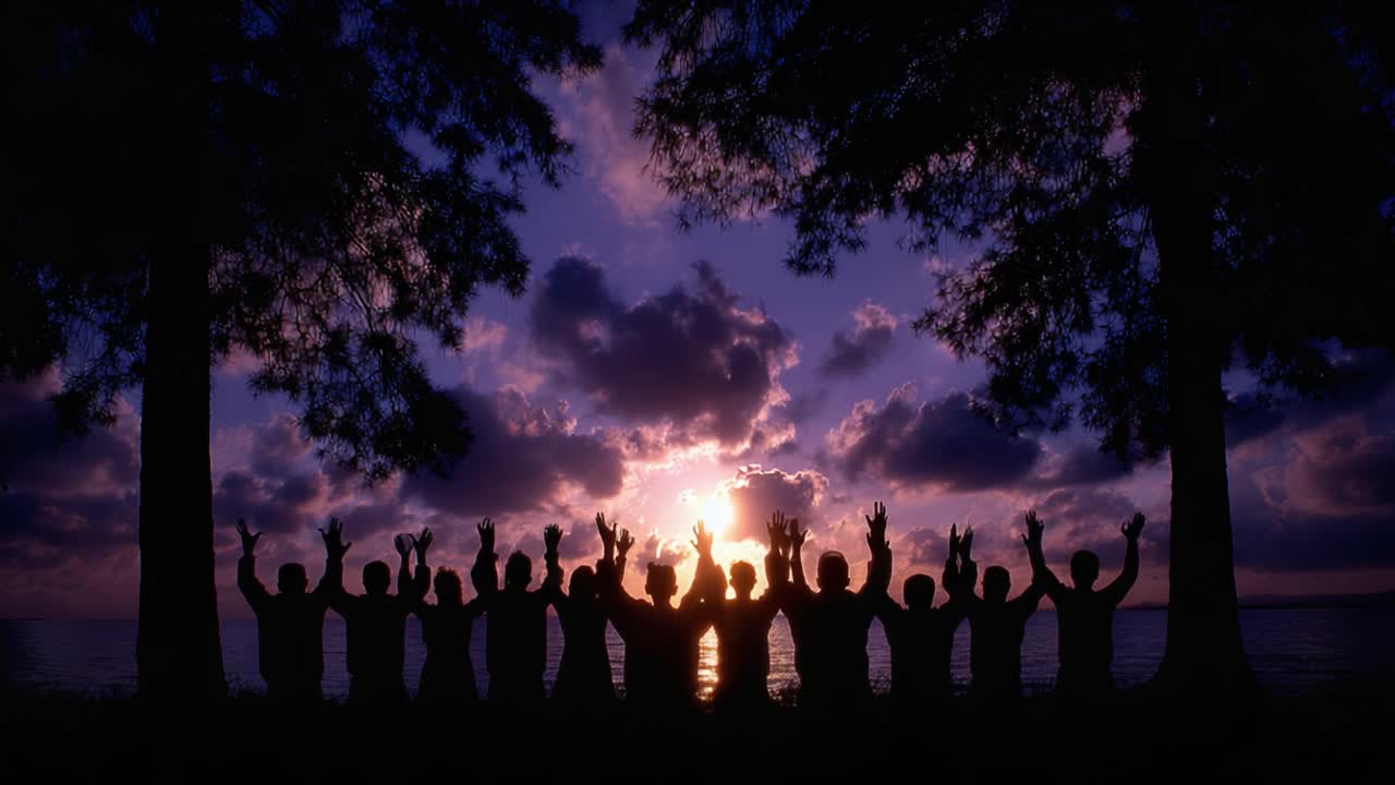 A group of silhouetted individuals joyfully raising their hands against a stunning sunset backdrop, capturing a moment of celebration and togetherness amid nature's beauty