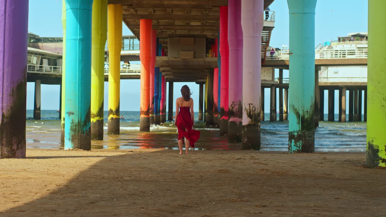 Woman in Red Dress Walking on a Colorful Beach Pier