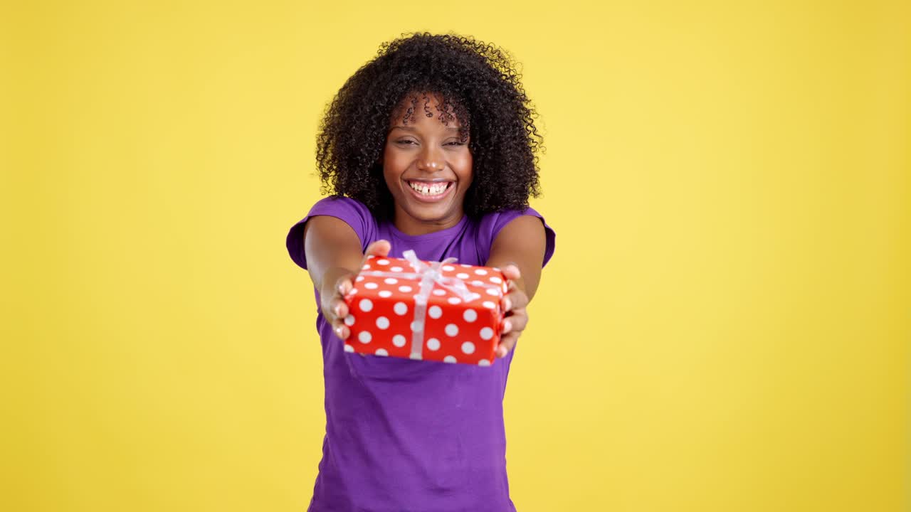 Happy woman posing and presenting a gift on a yellow background