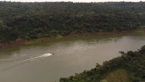 aerial tracking shot of speedboat cruising on idyllic river border between brazil and argentina surrounded by amazon river