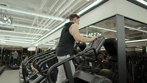 mature bearded muscular man doing cardio on stair climber machine in fitness center - low angle