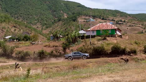 Grey-four-wheel-drive-open-back-truck-driving-on-a-dusty-road-with-a-trail-of-dust-plume-in-small-town-rural-countryside,-Timor-Leste,-Southeast-Asia