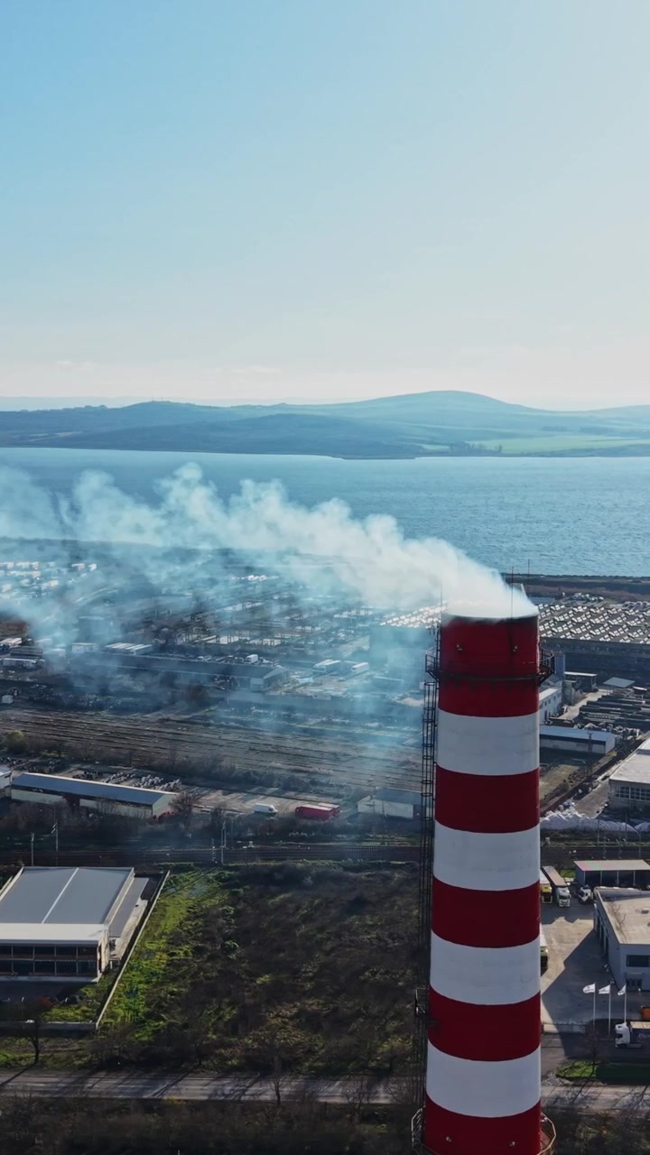 Smoke rises over industrial area near the coast during clear day