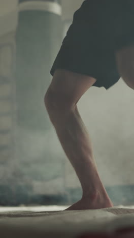 Sportsman jumps kicking punching bag in sports club closeup. Professional kick-boxer exercises with heavy equipment in gym slow motion. Martial arts