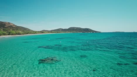 Drone-flying-through-trees-at-a-beach-with-turquoise-water,-Corsica,-France