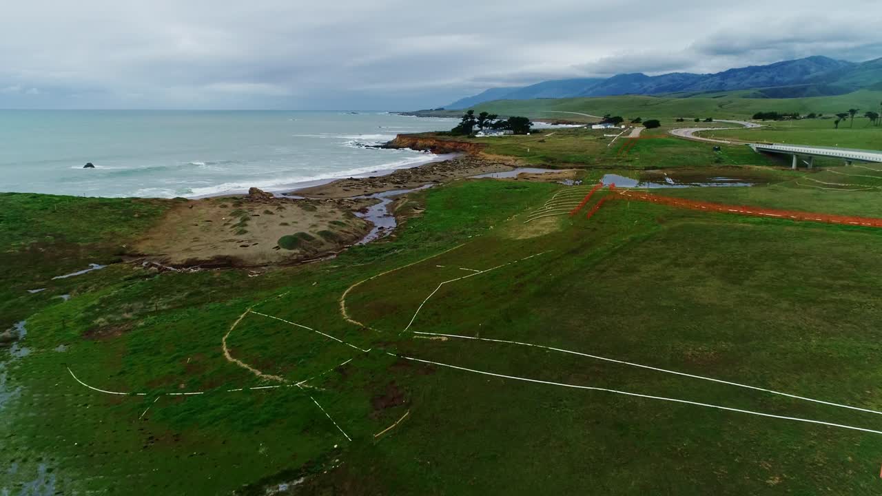 Misty green pastures stretch along rocky coastline, waves crashing near cliffs