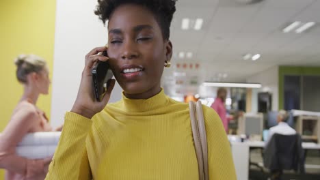 Happy-african-american-businesswoman-talking-on-smartphone-and-walking-in-office