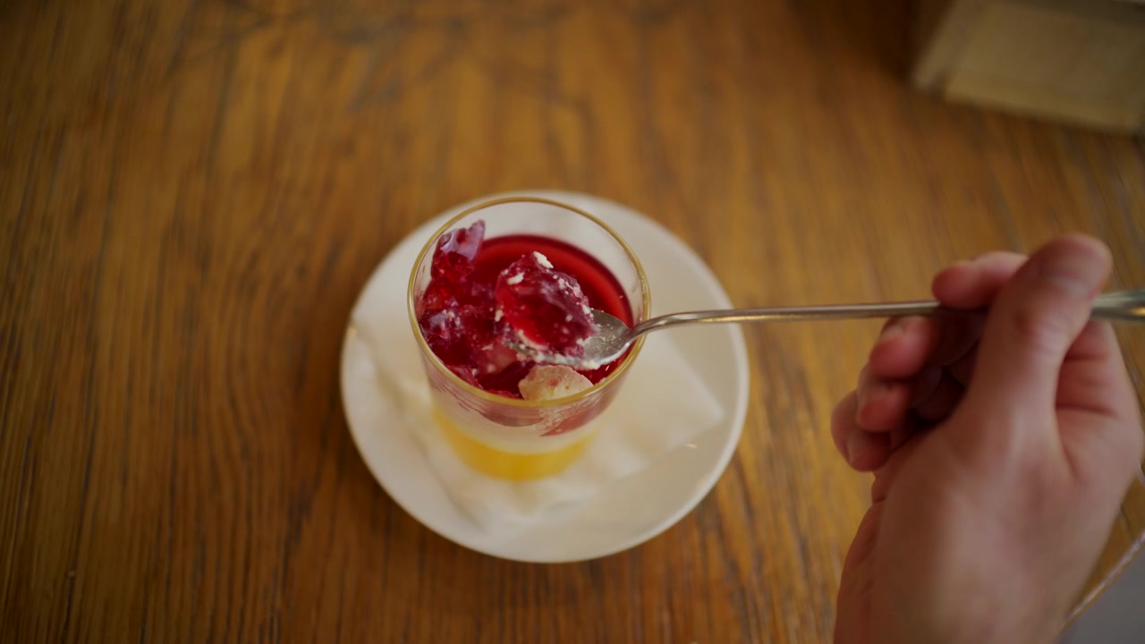 Primo piano di un cucchiaio che solleva un pezzo di gelatina di frutta rosso vivo da una coppetta da dessert di plastica trasparente.