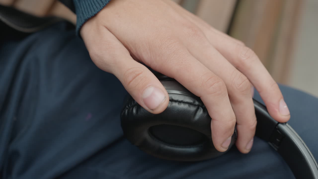 Nærbillede af en hånd, der justerer en høretelefon, forsigtige fingerspidser der føler på den slidte pude og det ridsede læder. Sekvensen viser reparation og inspektion af en audiotekniker, en musiker der tuner udstyr og en pendler, der piller.