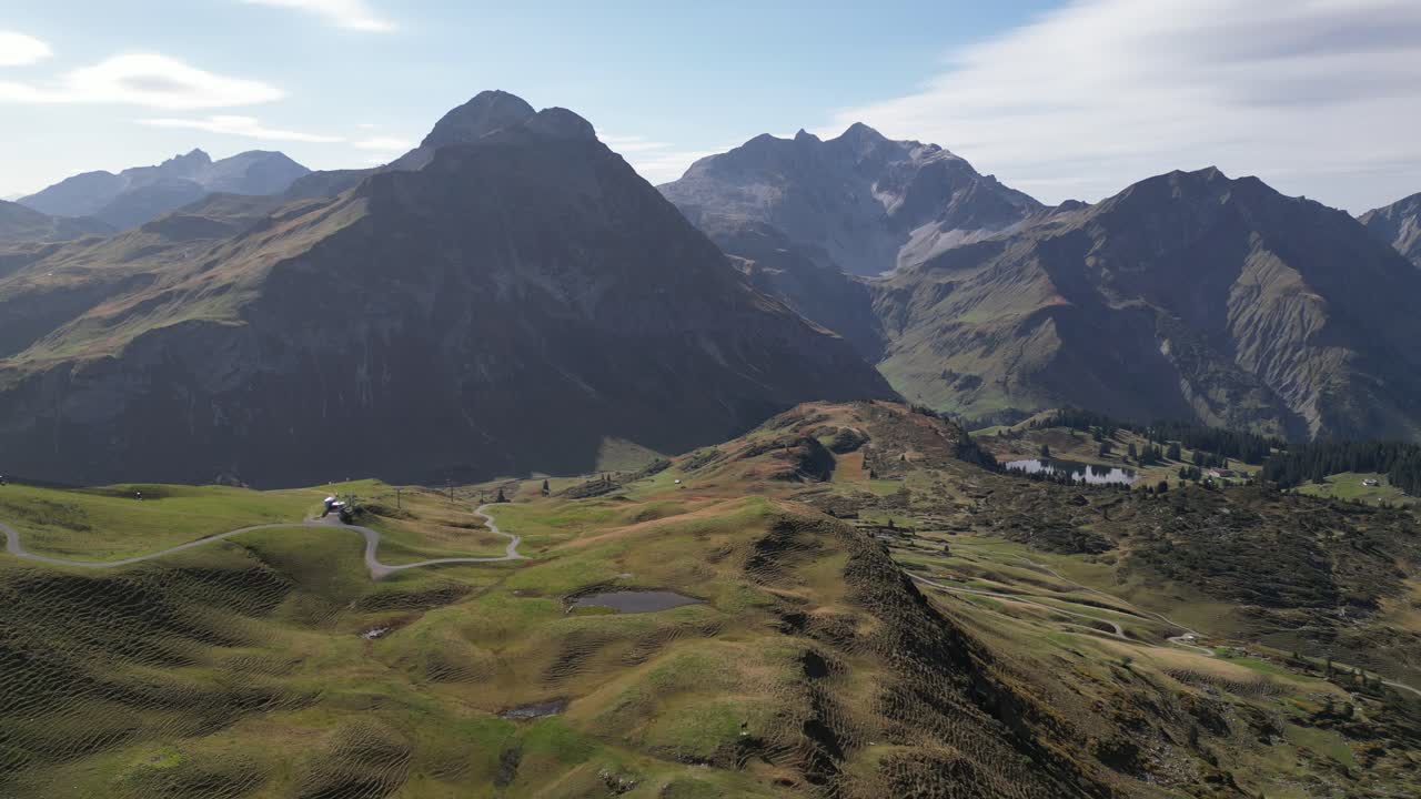 una impresionante vista aérea de colinas verdes y un camino sinuoso en los alpes austriacos cerca de arlberg y warth, con impresionantes paisajes de montaña y un cielo despejado salpicado de nubes ligeras