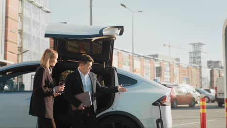 business people discussing by an electric car
