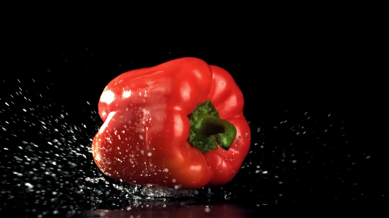 Červená paprika padající a stříkající voda na černém pozadí.