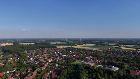housing area between green trees and farm fields in america. blue sky with wind turbines in distance. red and orange tiles on roofs of homes in small town of usa. aerial wide shot.
