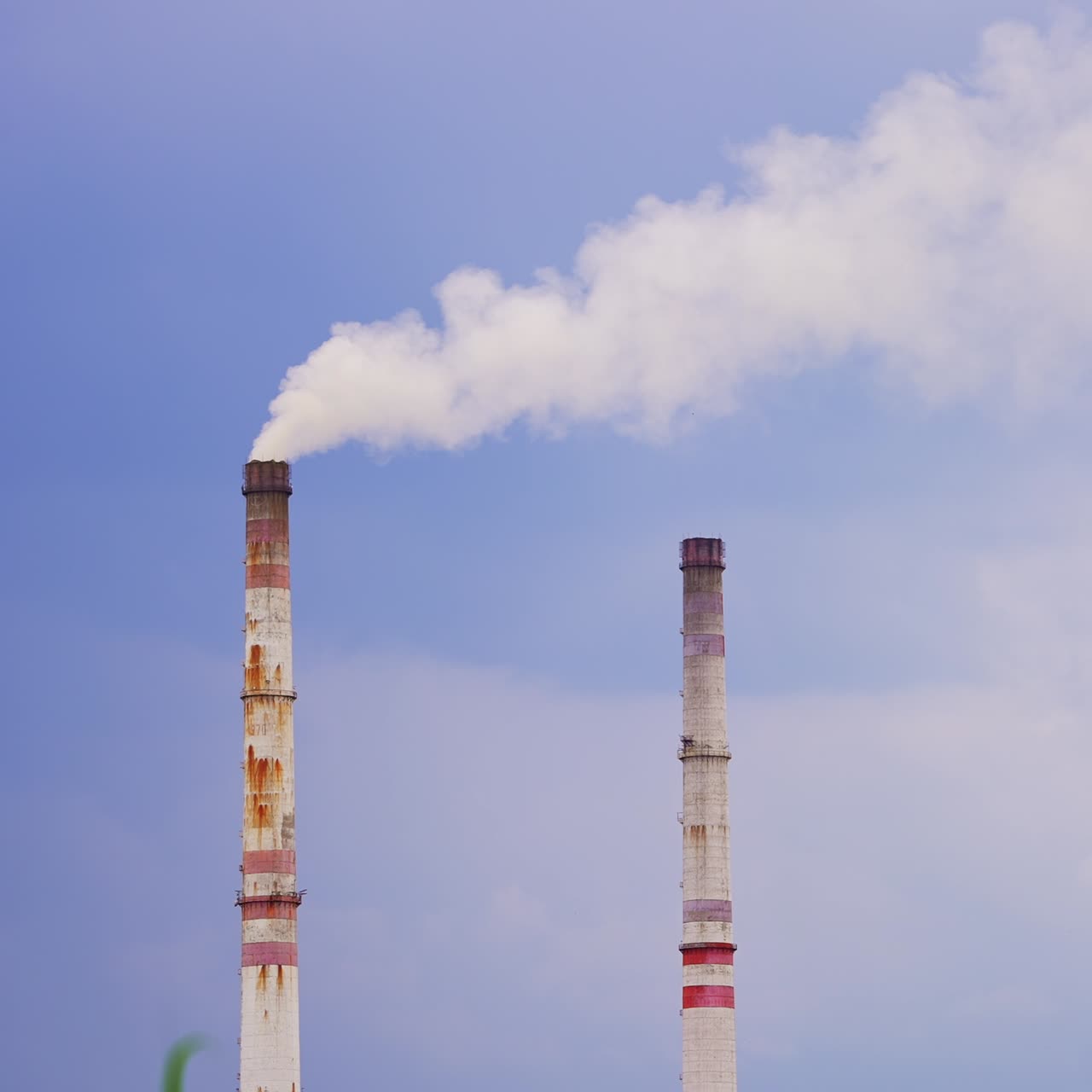Plant pipes producing white smoke into air. Industrial smoke polluting atmosphere. Blue sky backdrop