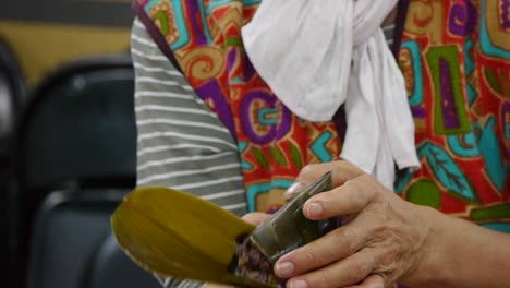 manos de mujer envolviendo el tradicional triángulo de arroz morado en un recipiente de hojas durante la preparación de alimentos, filmadas de cerca