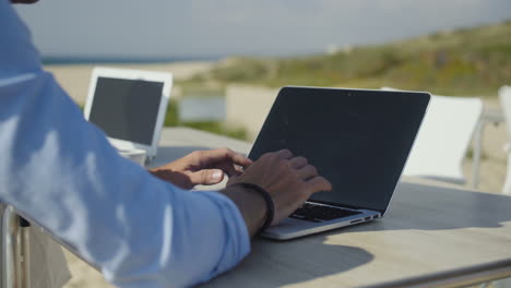 cropped shot of couple using laptops on beach