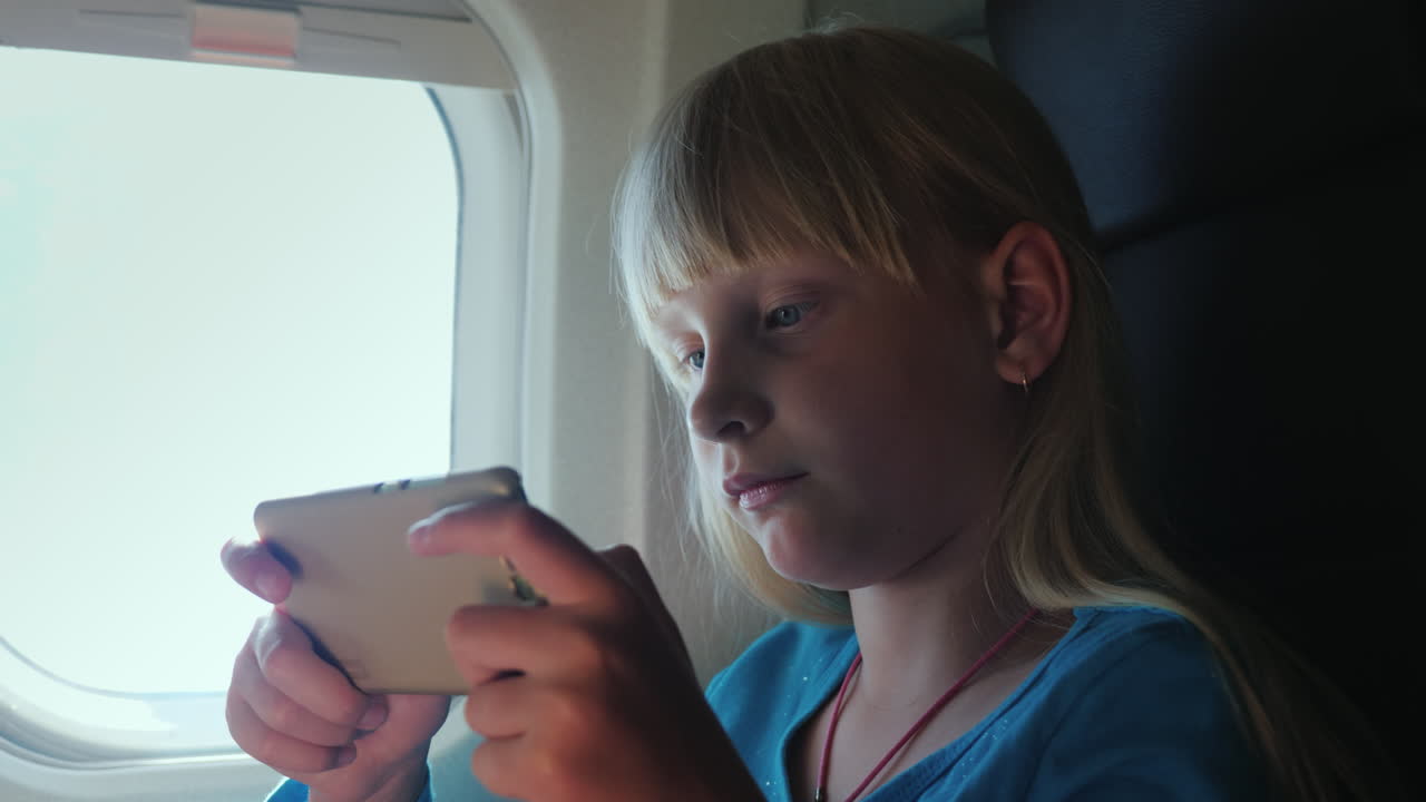 una chica rubia juega en un teléfono inteligente mientras vuela en un avión