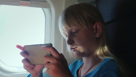 a blonde girl plays on a smartphone while flying in an airplane