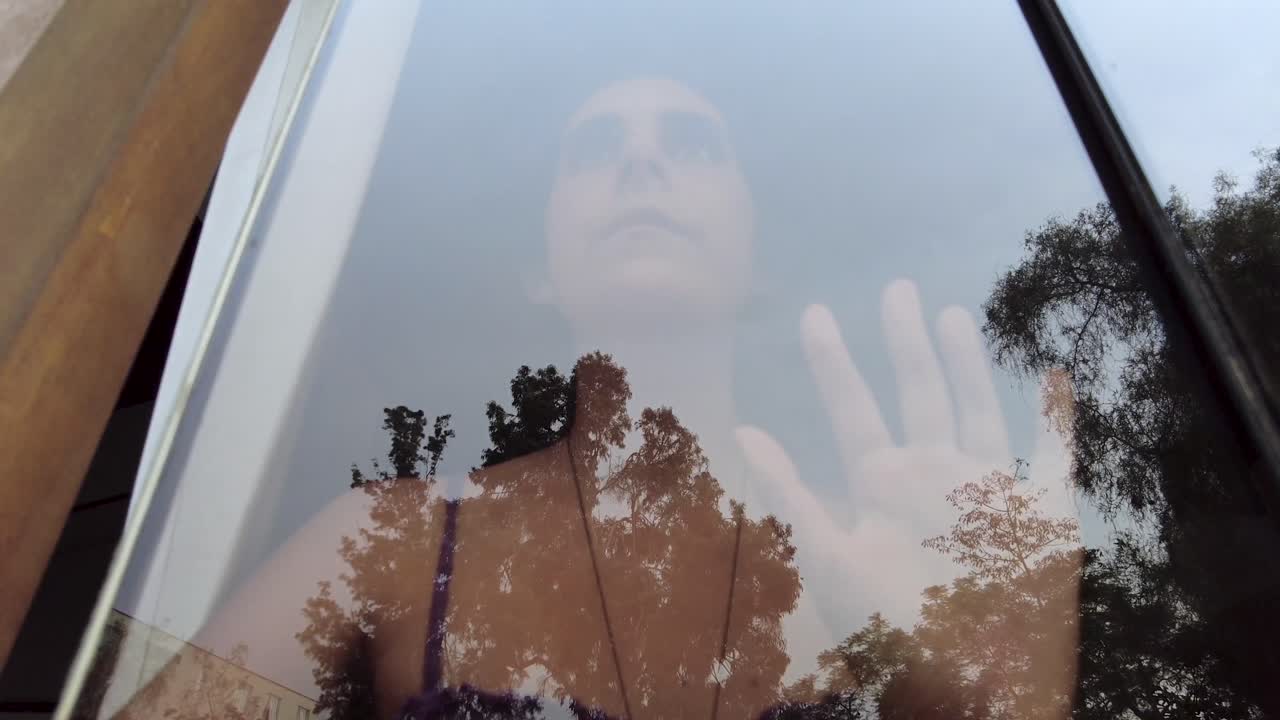 joven triste detrás de una ventana de vidrio, sintiéndose atrapada sufriendo de depresión, encierro