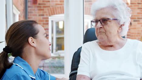 Senior-Woman-Sitting-In-Motorized-Wheelchair-Talking-With-Nurse-In-Retirement-Home