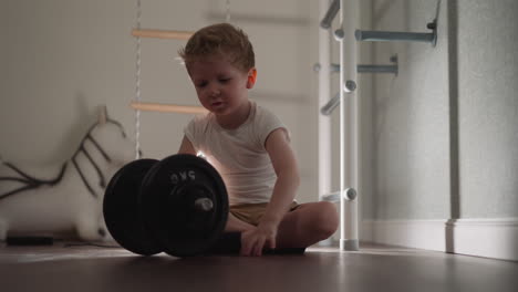 curious little boy examines heavy barbell for workout