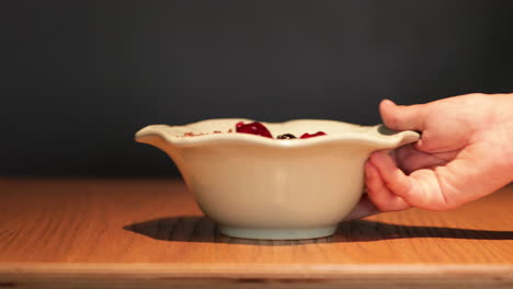 mano sirviendo un tazón de cereal de frutas sobre una mesa de madera con fondo negro - primer plano