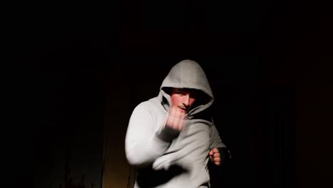 человек в капюшоне боксирует под драматическим прожектором с черным фоном, интенсивная фокус.