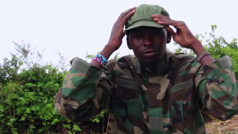 sad army man, sitting in jungle, fixing hat and puts hands on face, cloudy day