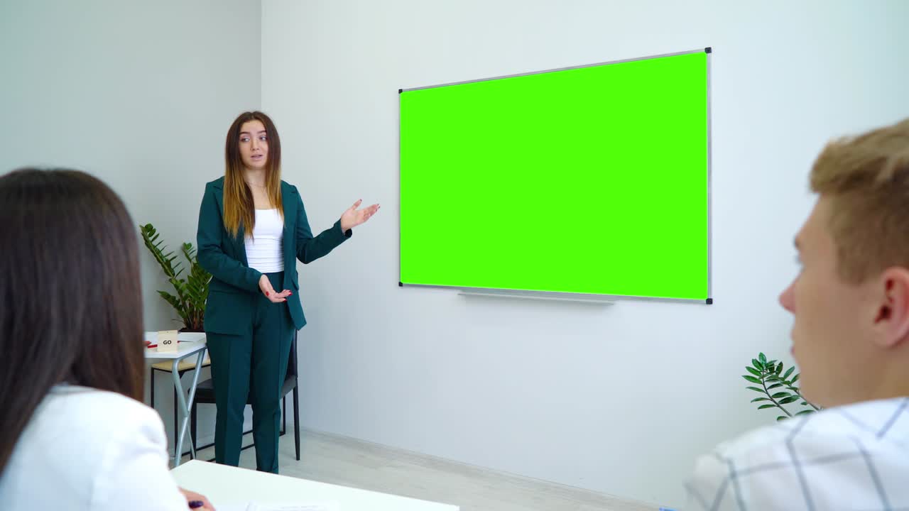 joven maestro feliz cerca con un tablero de pantalla verde enseñando a los estudiantes en el aula