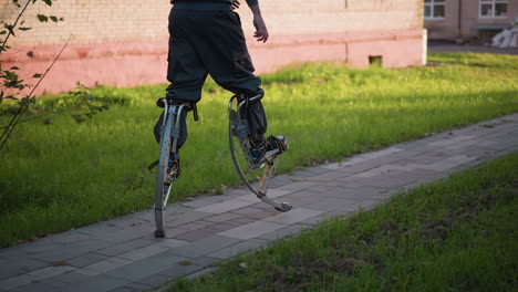 person walking on stilts wearing gray hoodie and pants on paved road surrounded by green grass and trees, showcasing balance, agility, and dynamic motion, with an outdoor setting