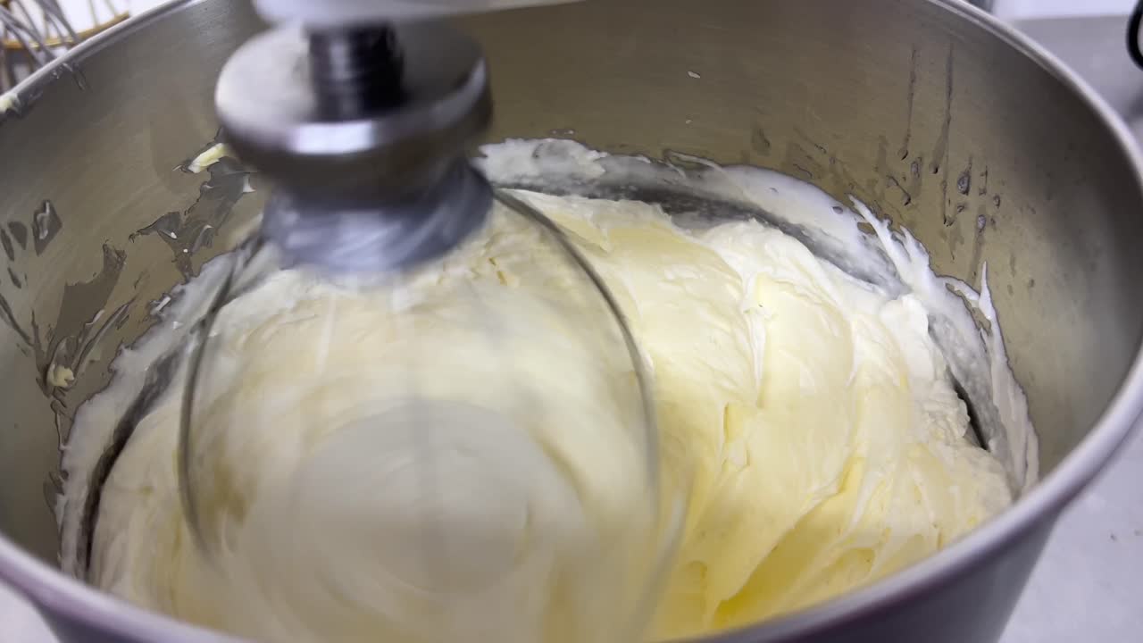 Fluffy and soft Swiss meringue buttercream pastry, electric mixer mixing and beating egg white and sugar until it is glossy peak and stiff peak, close up shot