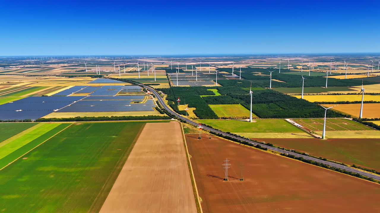 Bright sun lights the endless fields with solar panels and wind turbines. Aerial perspective on the plantations used for production green energy