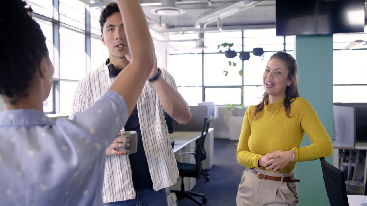 Colegas de trabalho diversos iniciando revisão de tarefas rolando tablet na estação de trabalho, bebendo de uma caneca.