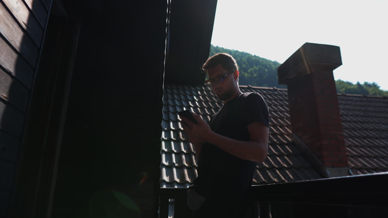 지붕의 발코니에서 스마트폰을 사용하는 남자