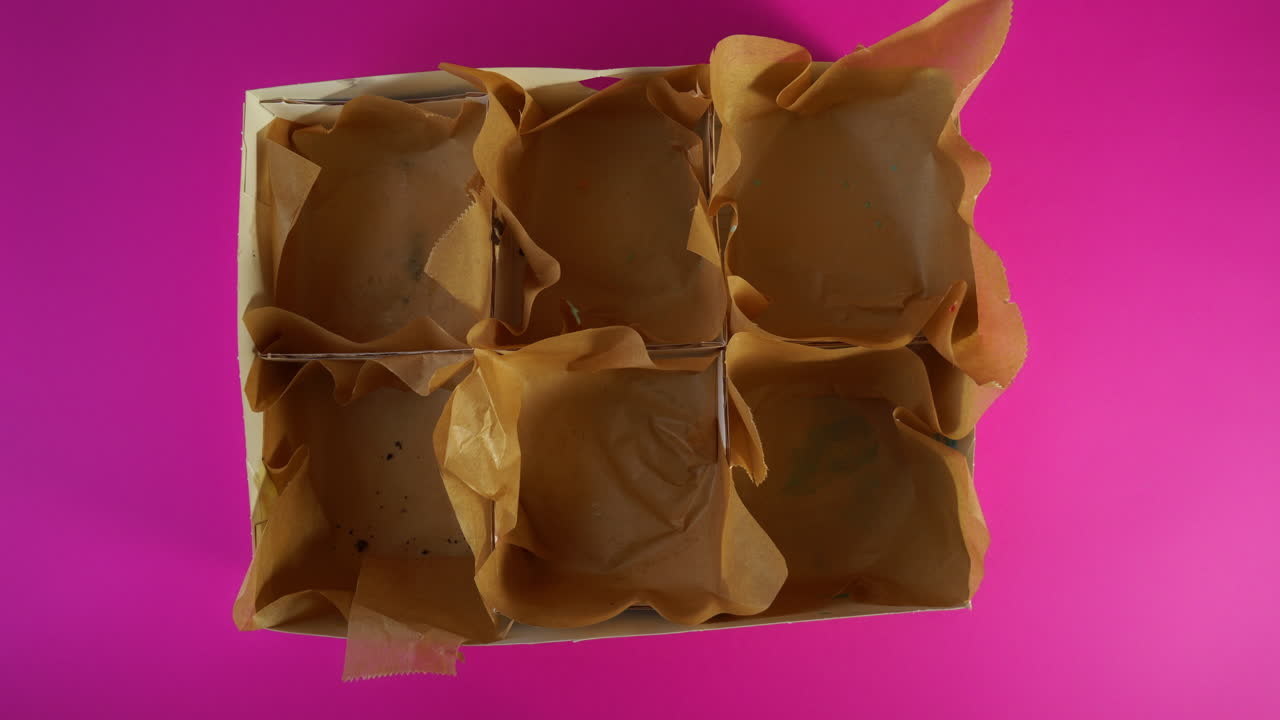 A six-slot delivery box is filled one by one with colorful donuts—featuring marshmallows, gummy shark, mochi, sprinkles, and cookie crumble—in a playful stop motion sequence. vibrant pink background