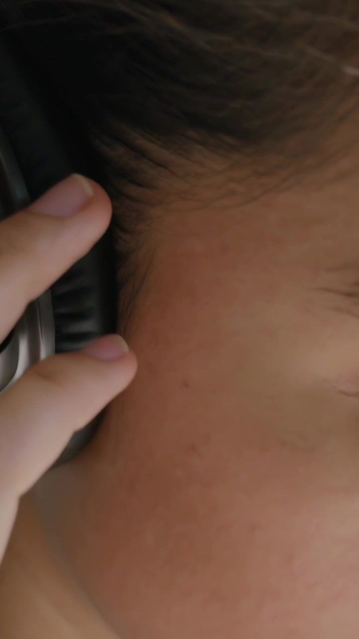 Video verticale: Donna che aggiusta le cuffie in una stanza, una mano entra per sistemarle meglio, indossa un top chiaro.